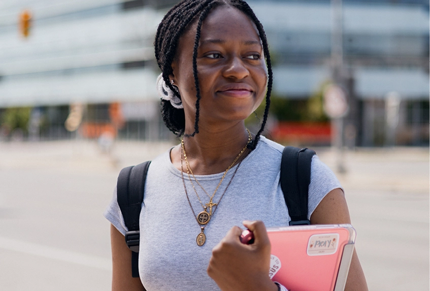 A student in a white shirt holding a pink tablet smiles towards camera