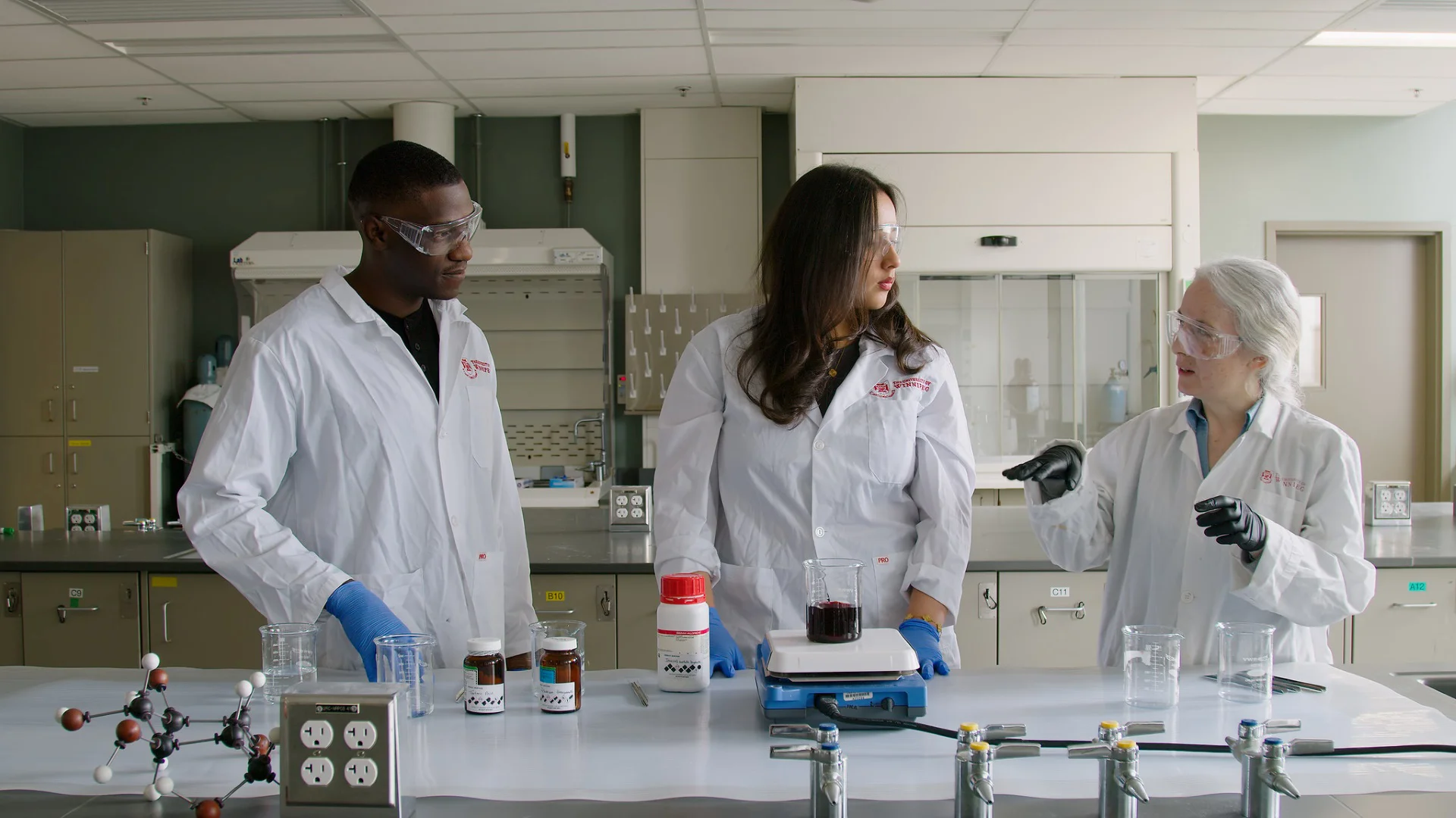 Faculty member talking to two students in a lab. All wearing labcoats.