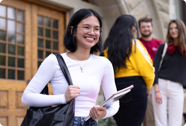 Student standing on front steps holding books and smiling