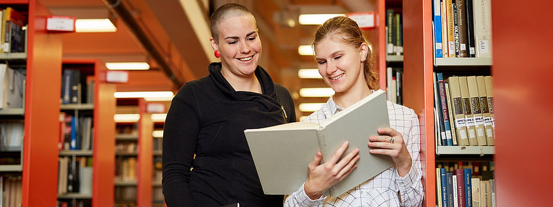 Students in library stand and look at book