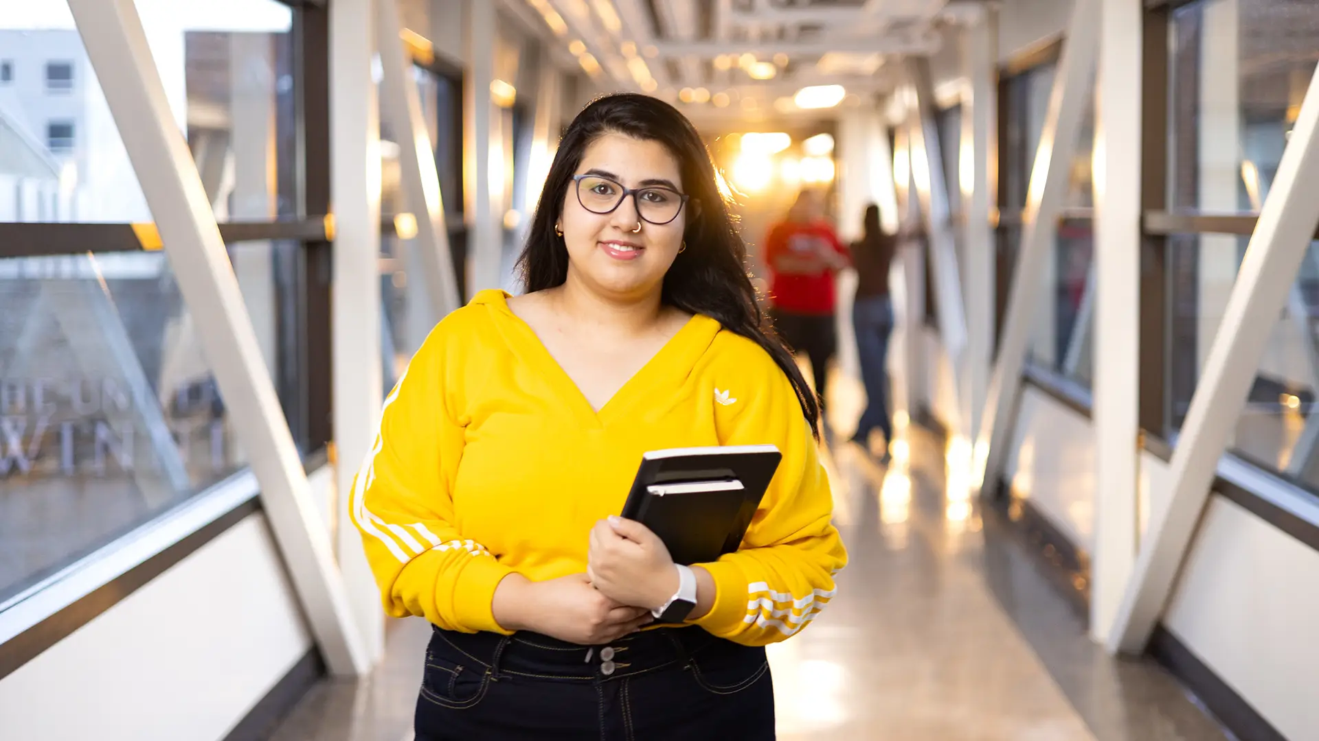 Student standing in the hallway, holding books and looking at the camera
