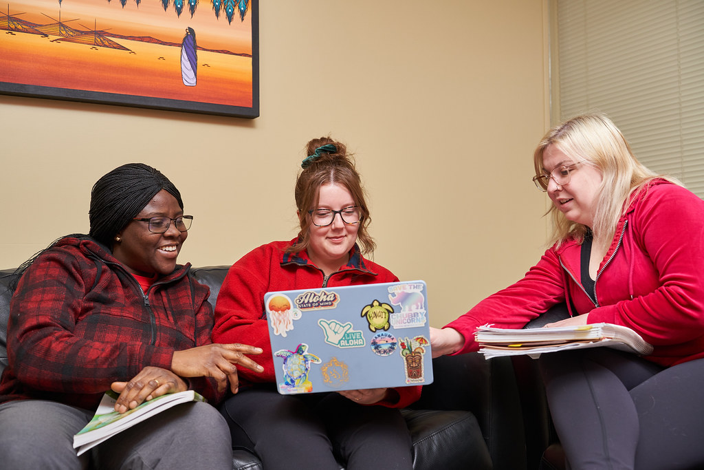 Three people sitting on couches looking at a laptop and talking.