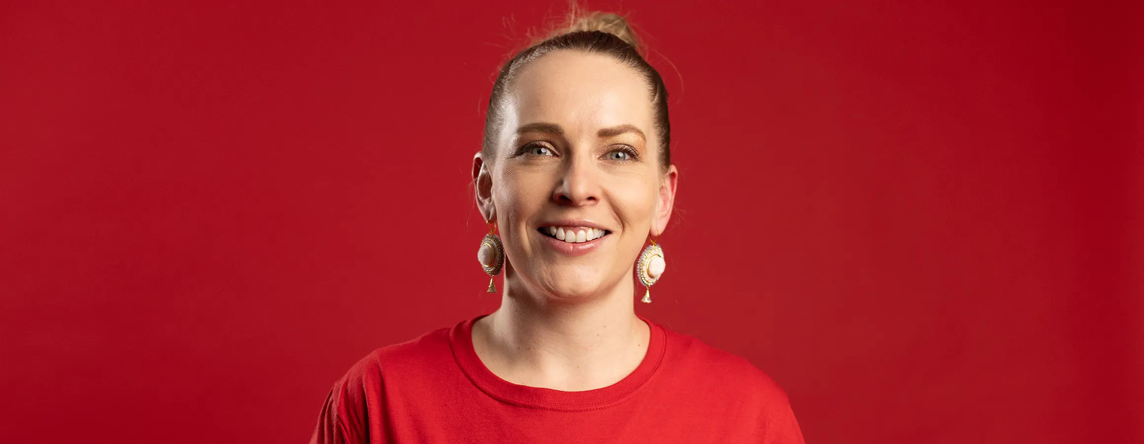 Headshot of a woman in a red shirt on a red background, smiling at camera.