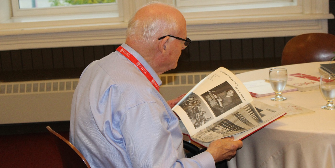 A person, with back to camera, is seated at a table looking through a yearbook.