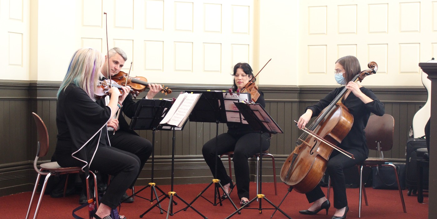 A four-piece string section plays music while atop a small stage.
