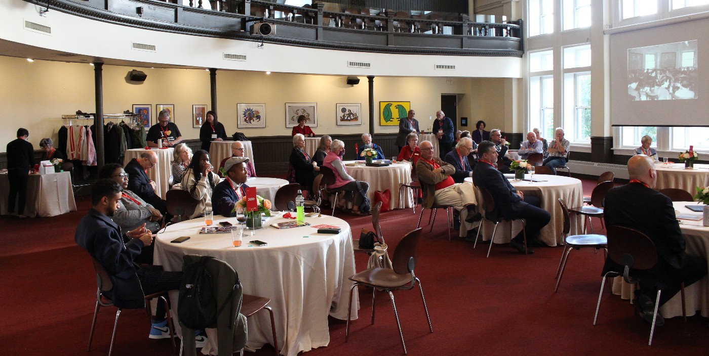 A wide shot of Convocation Hall shows Alumni Reception guests seated at round tables covered in white tablecloths.