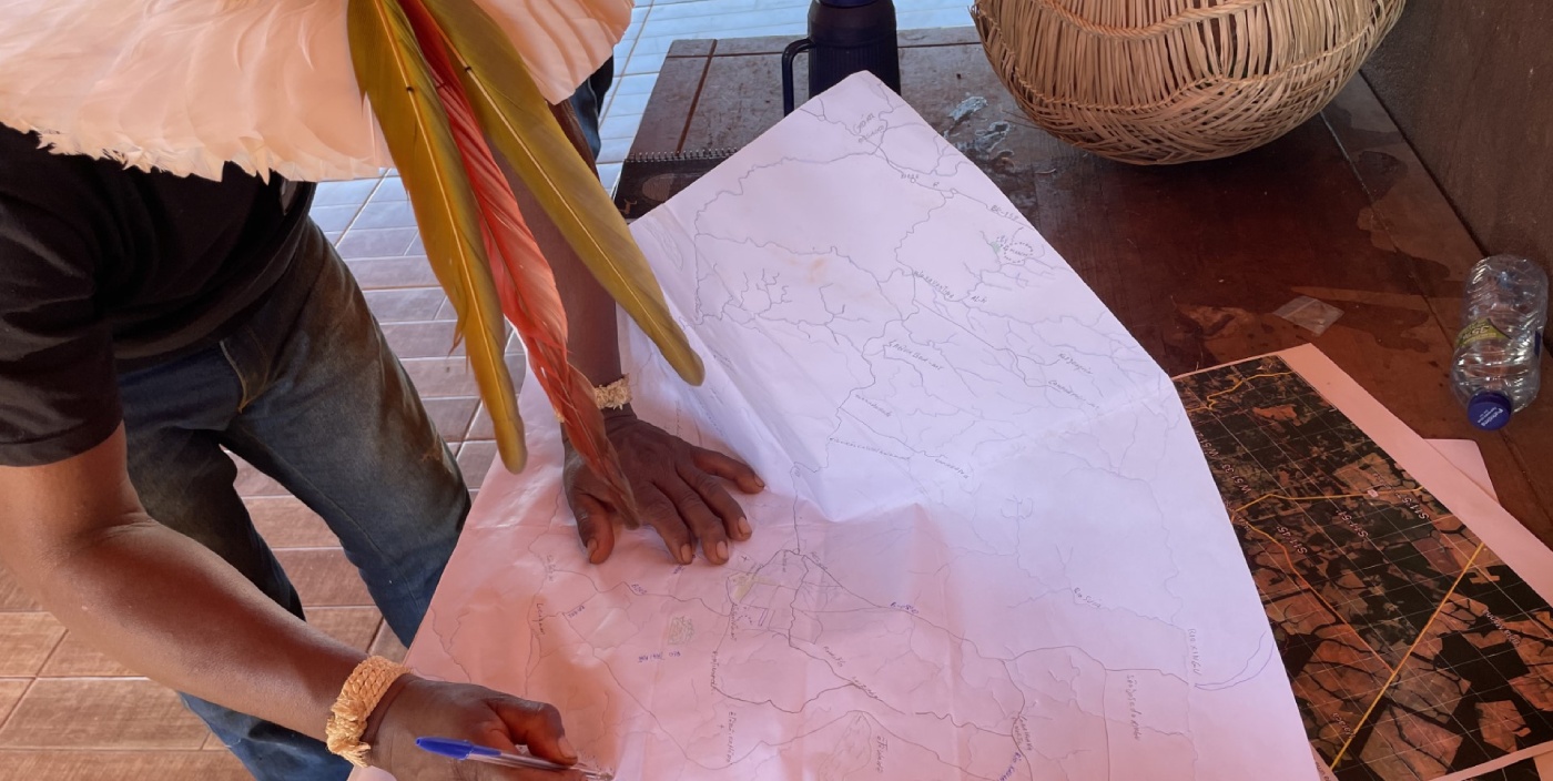 A person wearing a hat with large feathers looks down while sketching on a map