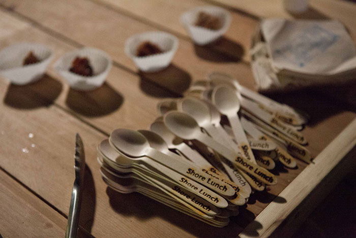 Spoons on a table with tongs, napkins, and food in paper cup cake liners