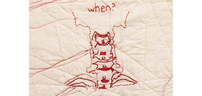Detail of cream-coloured quilt embroidered with red thread that shows part of a spinal column and the word "when?"