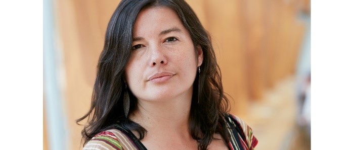 headshot of Wanda Nanibush facing the viewer in a fierce and confident way. She stands in front of a wood panelled wall that is blurred out in the background.