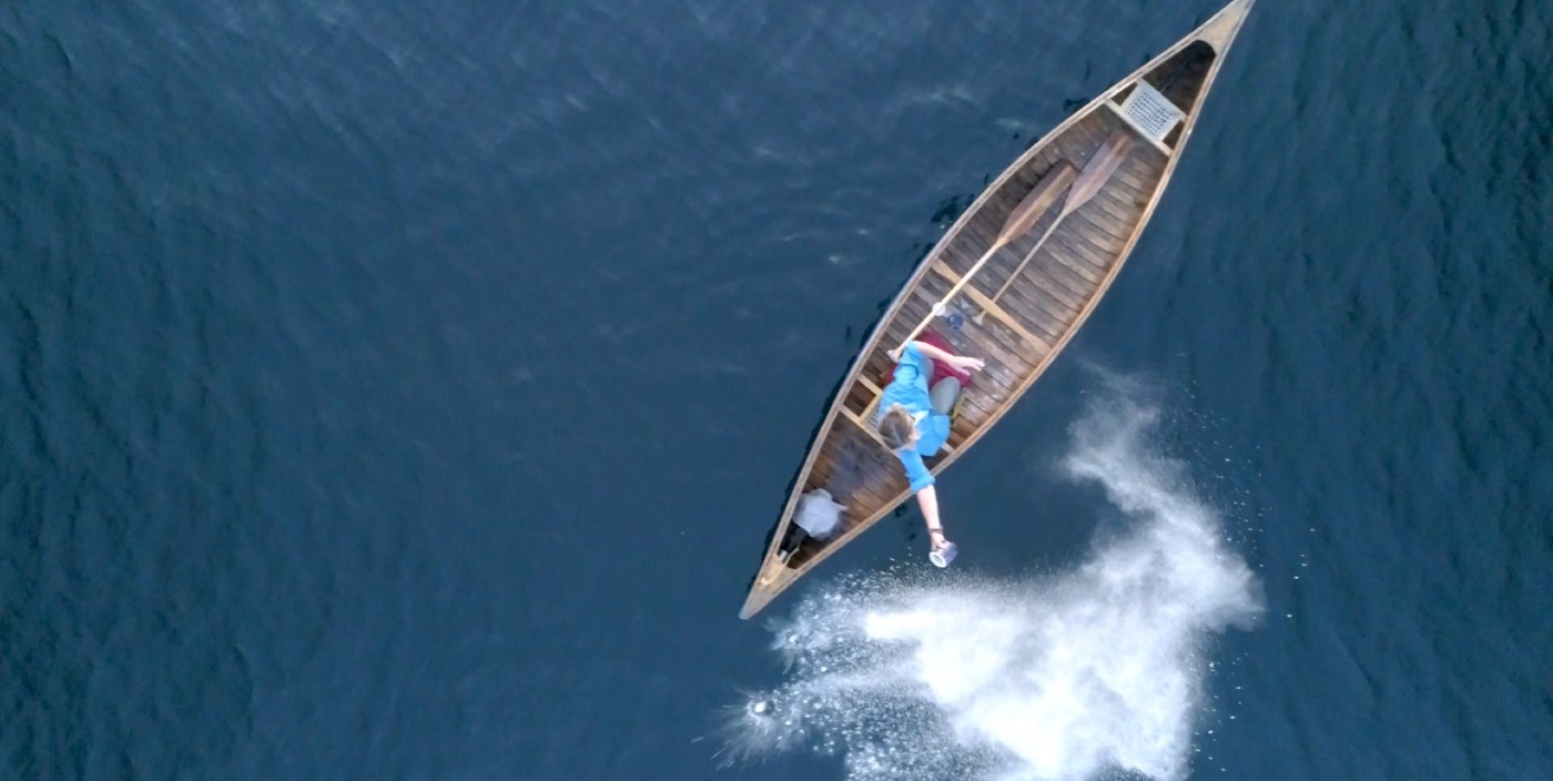Aerial photograph of a person in a canoe surrounded by a body of water. They are throwing cremains out of a cup into the water beside them.