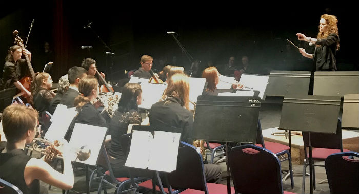 An orchestra sits facing a conductor in the midst of playing