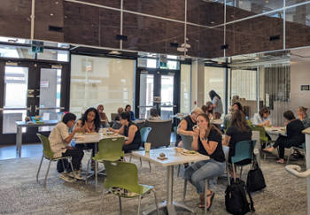 participants gather for lunch at small square cafe tables in a bright space at Merchants Corner