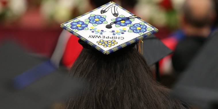 A graduate wearing a beaded graduation cap faces away from the camera