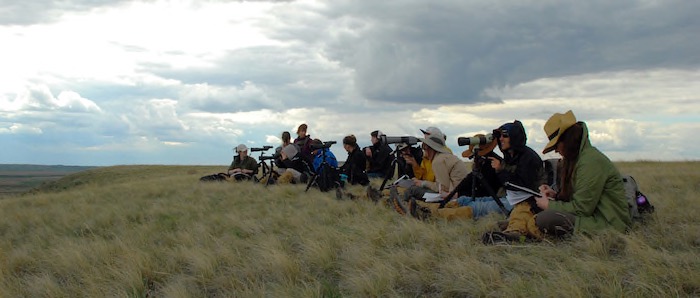 Students in a field with telescopes and notepads