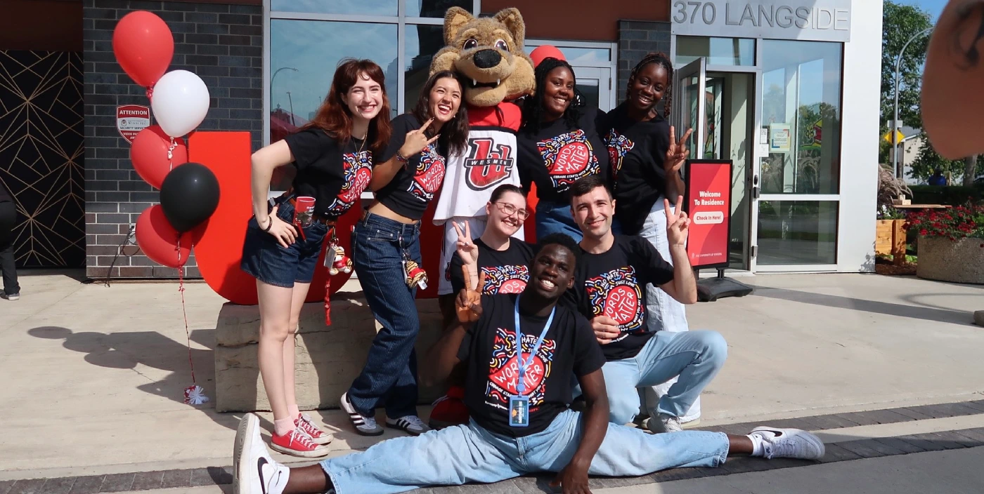 Several staff and UWinnipeg mascot Wes Lee Coyote outside McFeetors Hall