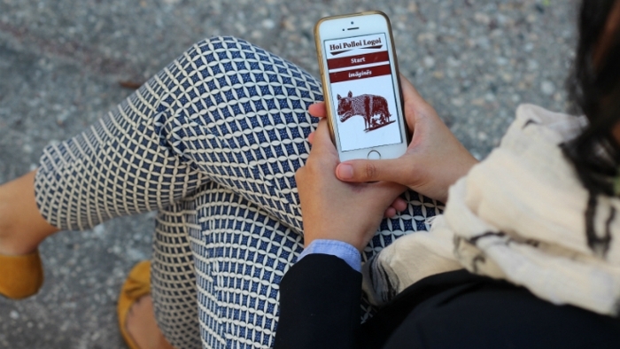 Student sitting on bench, using Hoi Polloi Logoi app on iPhone