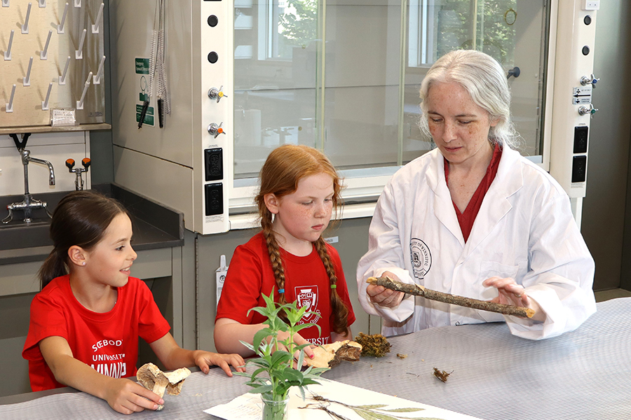 Two children are shown a science experiment by a professor in a lab coat