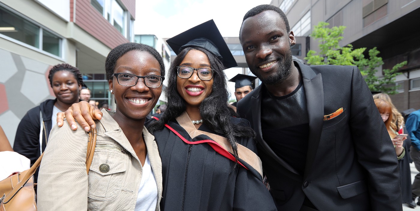 A graduating student smiling while being hugged by two guests