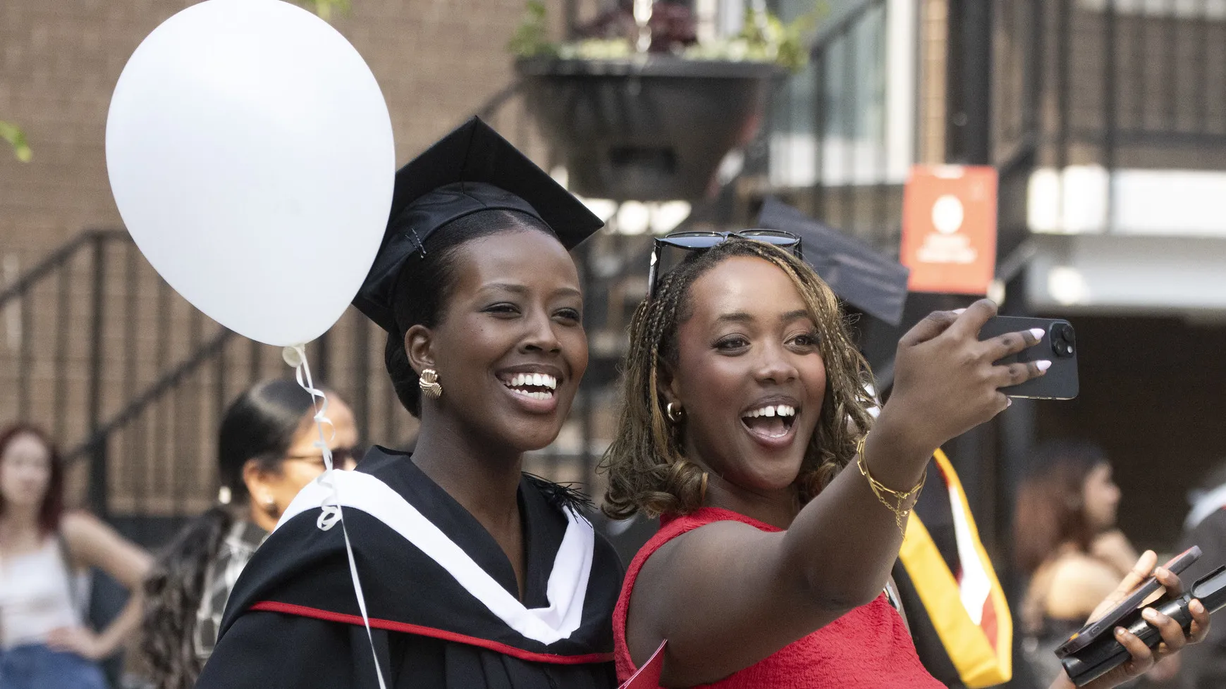Graduate holding balloon smiling with a friend taking a selfie