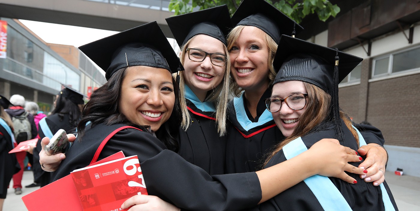 Four graduating students smiling as they embrace in a group hug