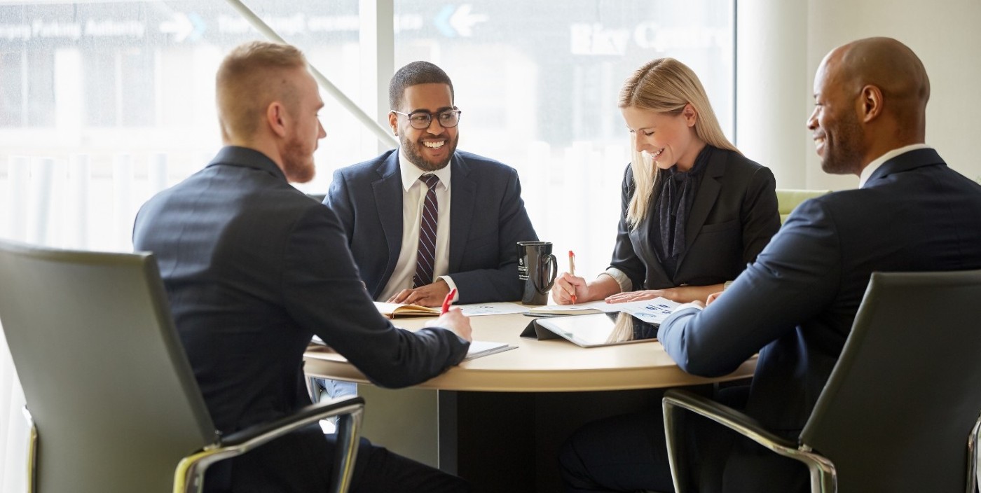 Several people sitting around an boardroom table speaking with each other