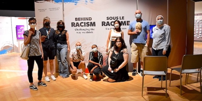 Image of a group of people in front of sign for Behind Racism exhibit