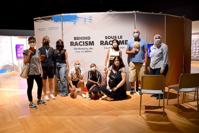 Nine people in front of "Behind Racism" exhibit
