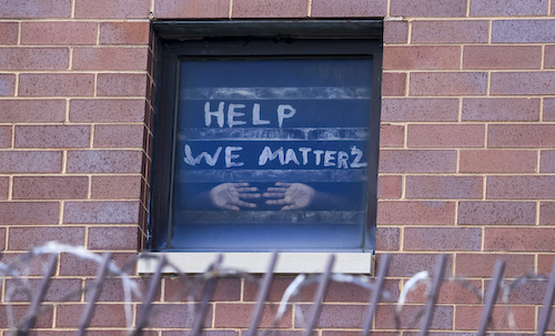 Image of an outside brick wall of a prison, with a window featuring two Black hands pressed against it and the text "Help We Matter 2."