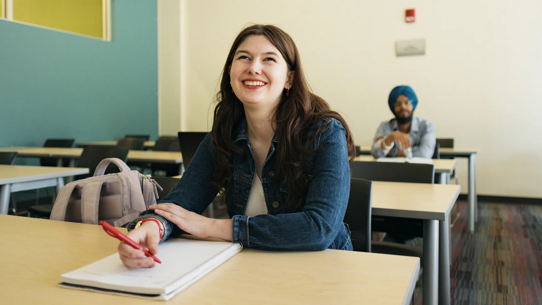 Student sitting at a desk holding a pen on a notebook, looking forward and smiling