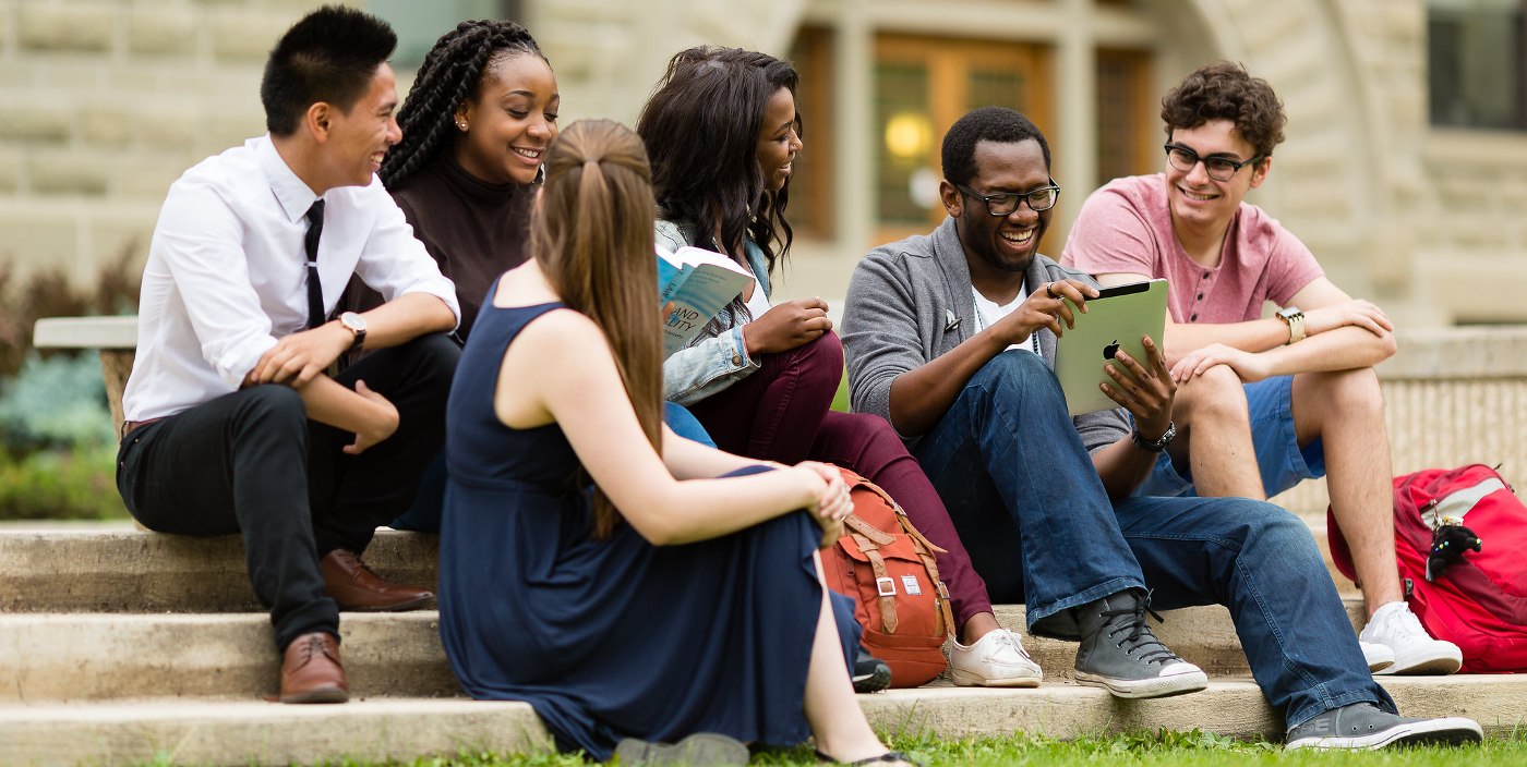 Diverse students sitting and meeting on the stairs outside The University of Winnipeg