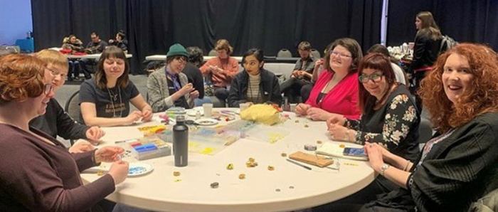 A diverse group of women sit around a table doing beading