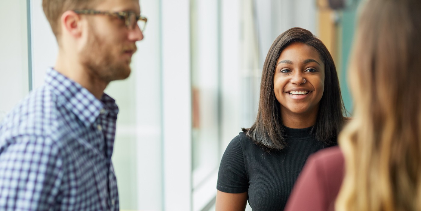 A student smiles while speaking with two others