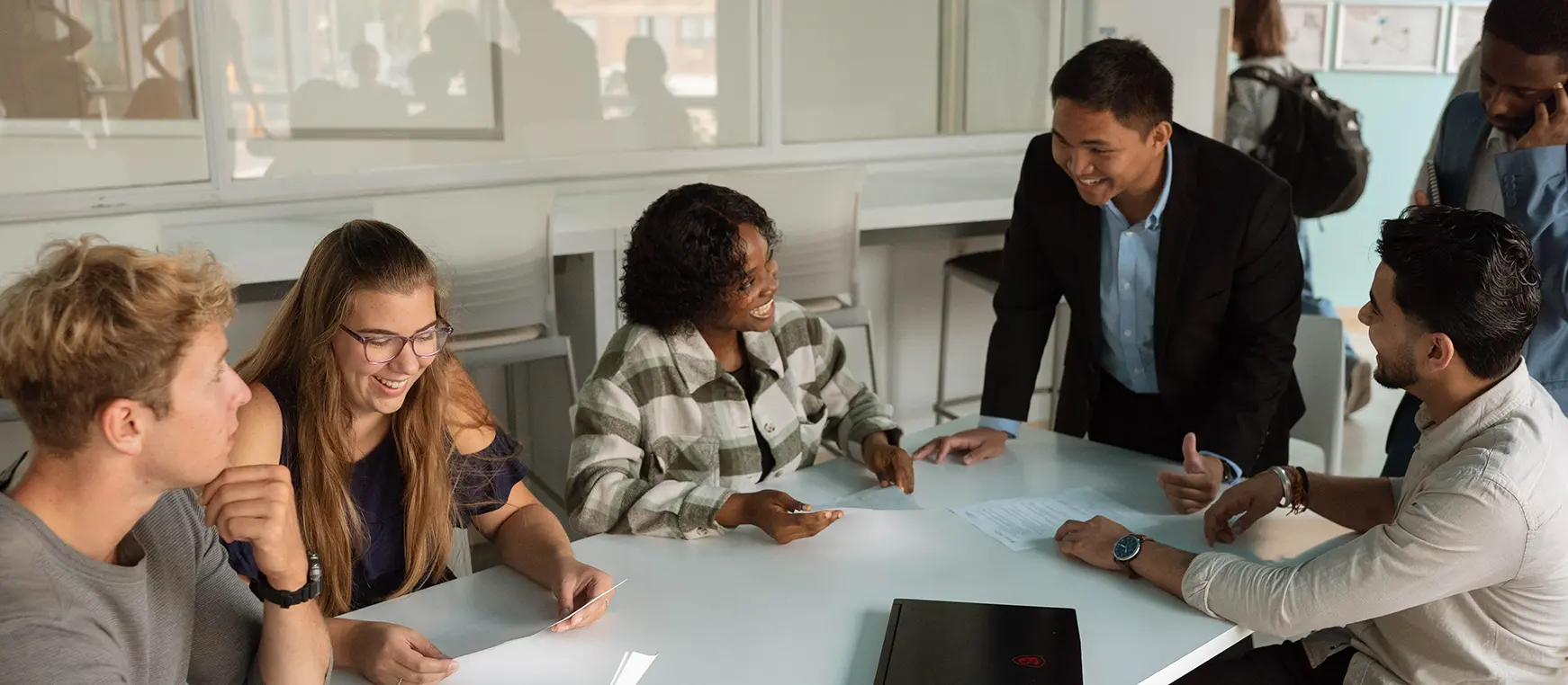 Several people in a boardroom, looking at papers, talking and smiling