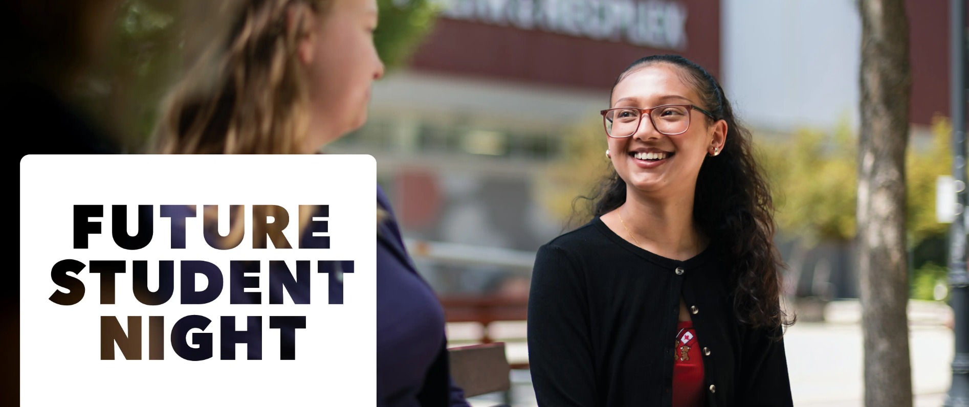 Three students sitting at a table outside smiling at the camera the words "Future Student Night" to the left