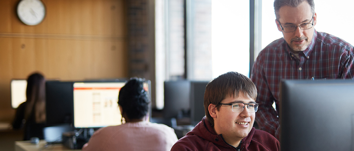 Student receiving assistance from staff in computer room.