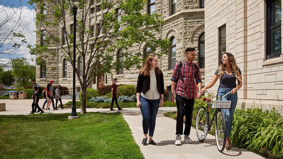 Three students walking on the UWinnipeg front lawn.