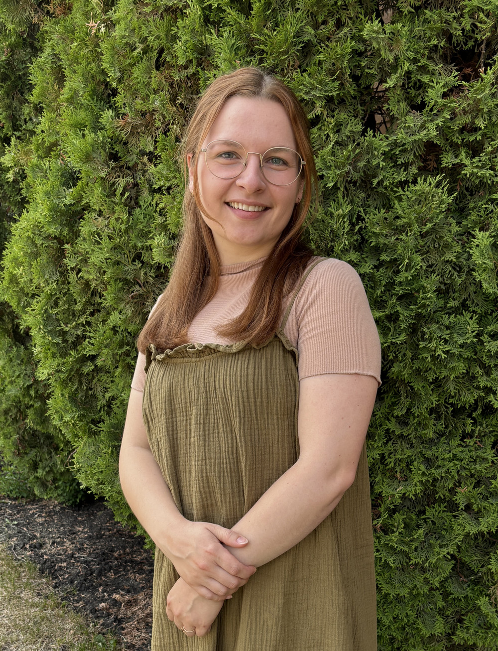 Lea Friesen stands in front of a shrub, smiling at the camera