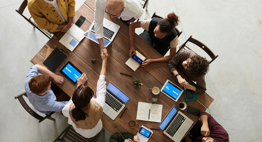 A bird's eye view of people gathered around a table with laptops and tablets visible. 