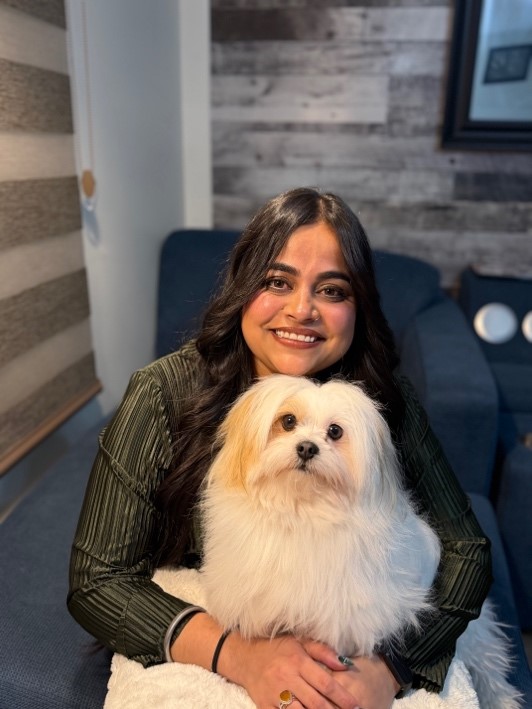 Abhijot Kaur Chohan smiling, a white fluffy dog is sitting oher her lap