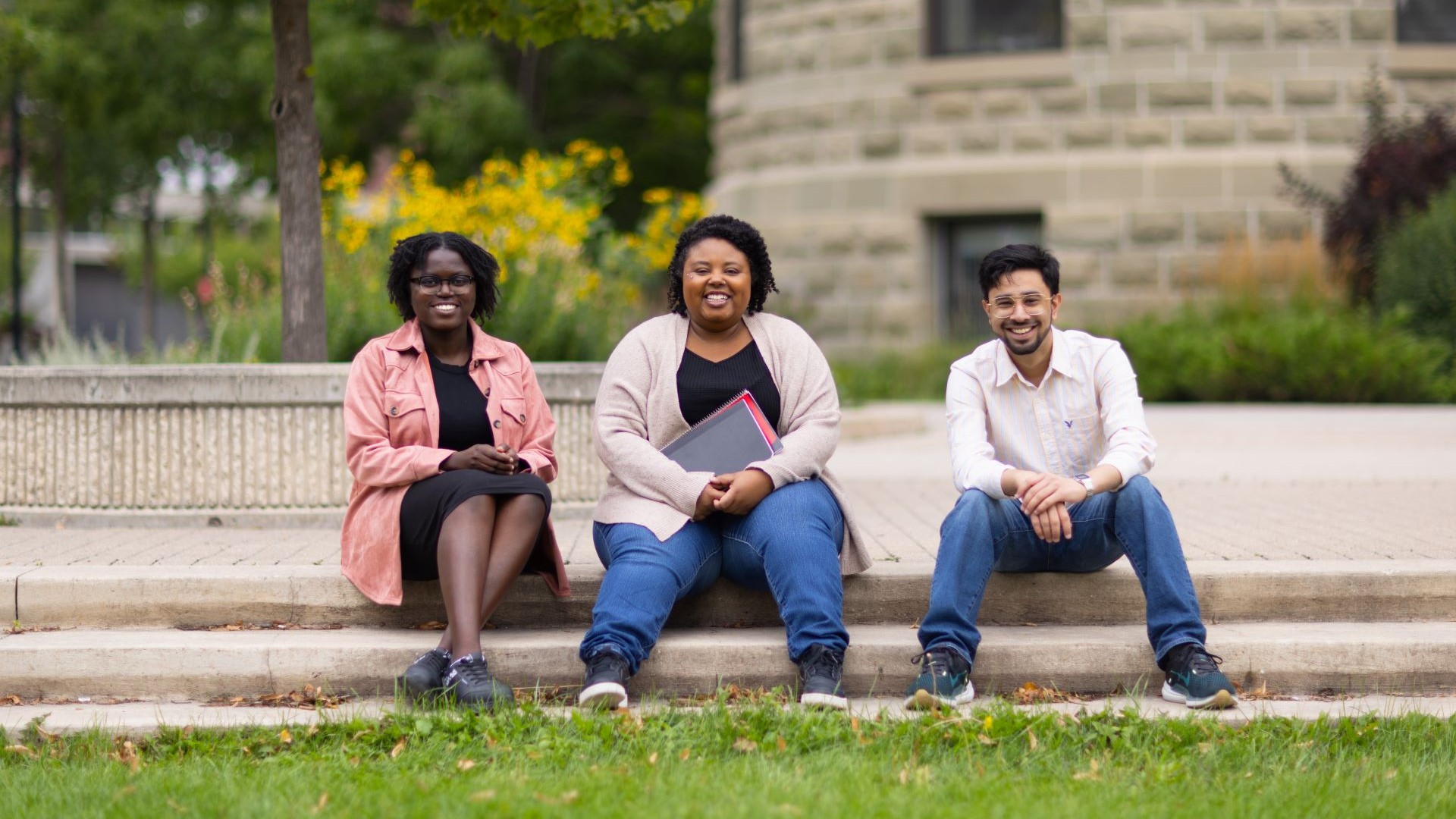 Three students sit in a row on The University of Winnipeg's campus. 