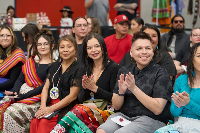 Students seated in a row. Some are wearing ribbon skirts, scarves, and beaded jewelry. 