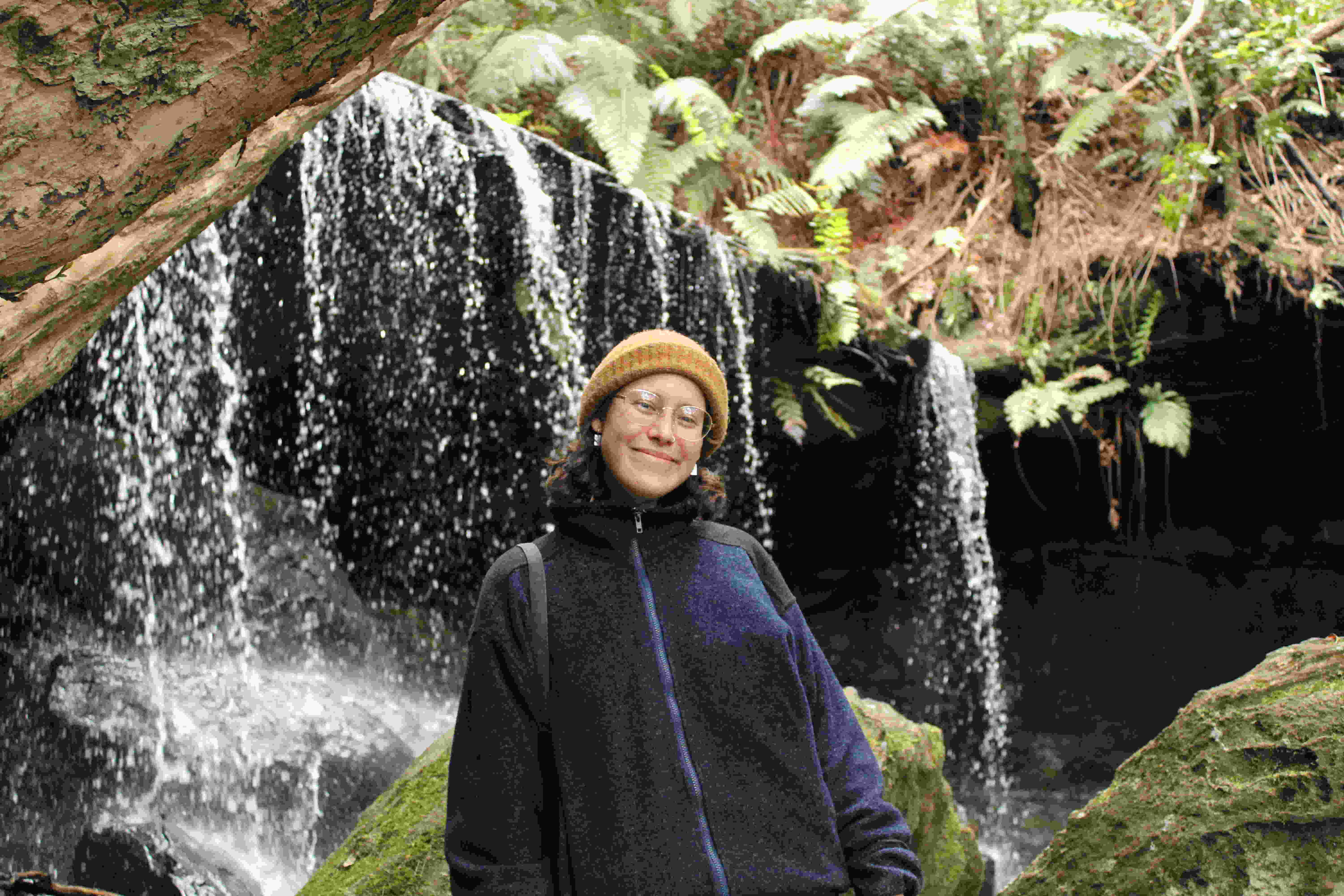 ISSP scholar Dominique stands smiling in front of a waterfall. 