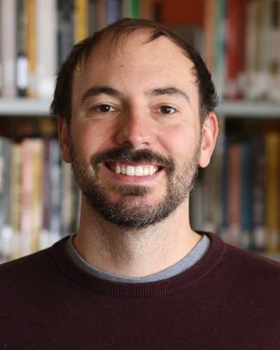 A headshot of Professor Jean-Pierre Desforges standing in front of bookcases full of books.