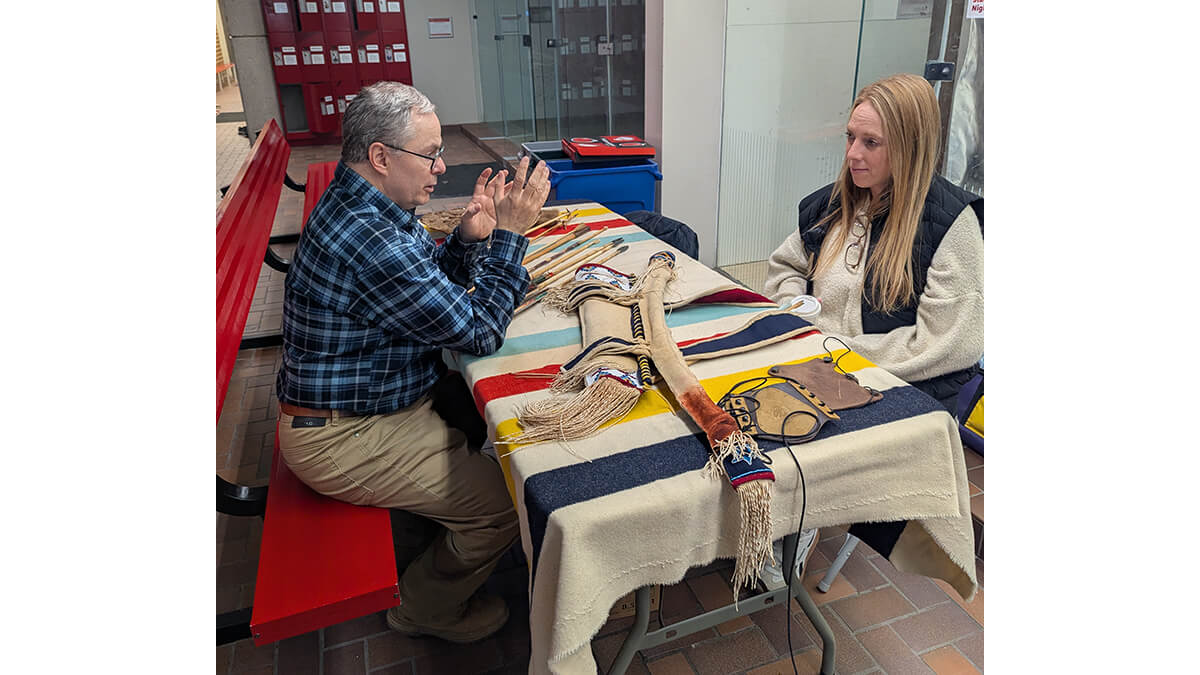 Two people either side of a table, talking. A Hudson's Bay blanket is on the table