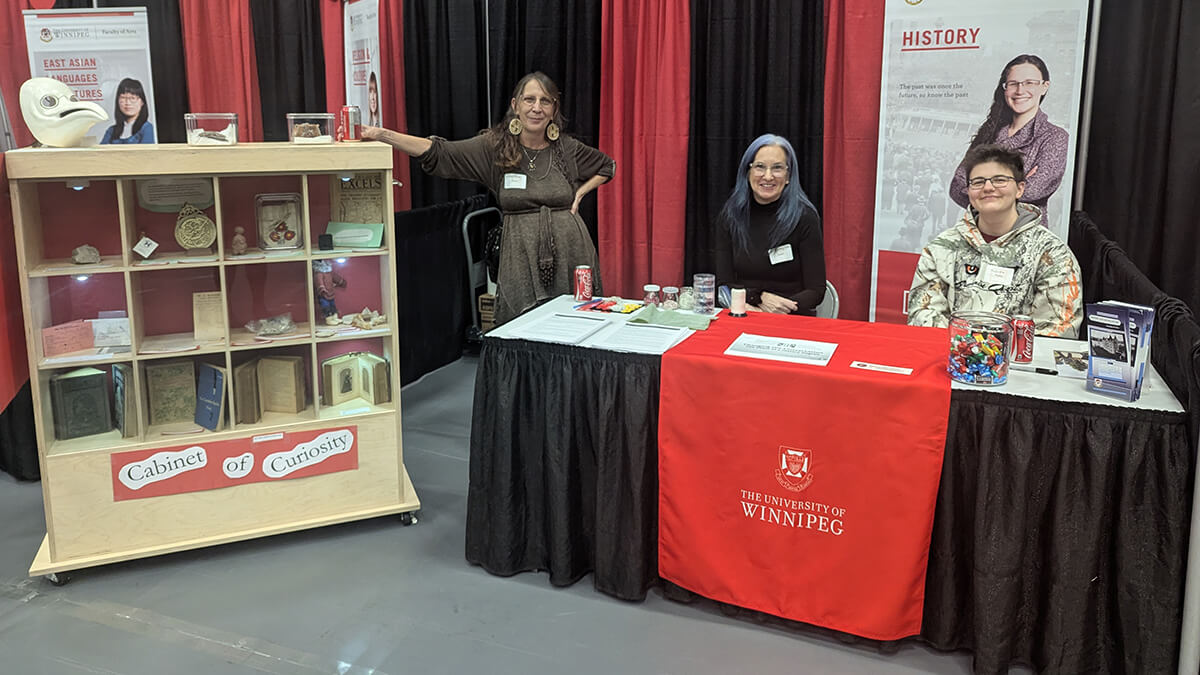 Two people sitting at a table and one standing, looking at the camera and smiling