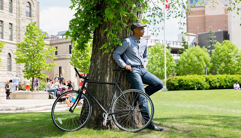 A man with a bike on Wesley Hall lawn leaning against a tree