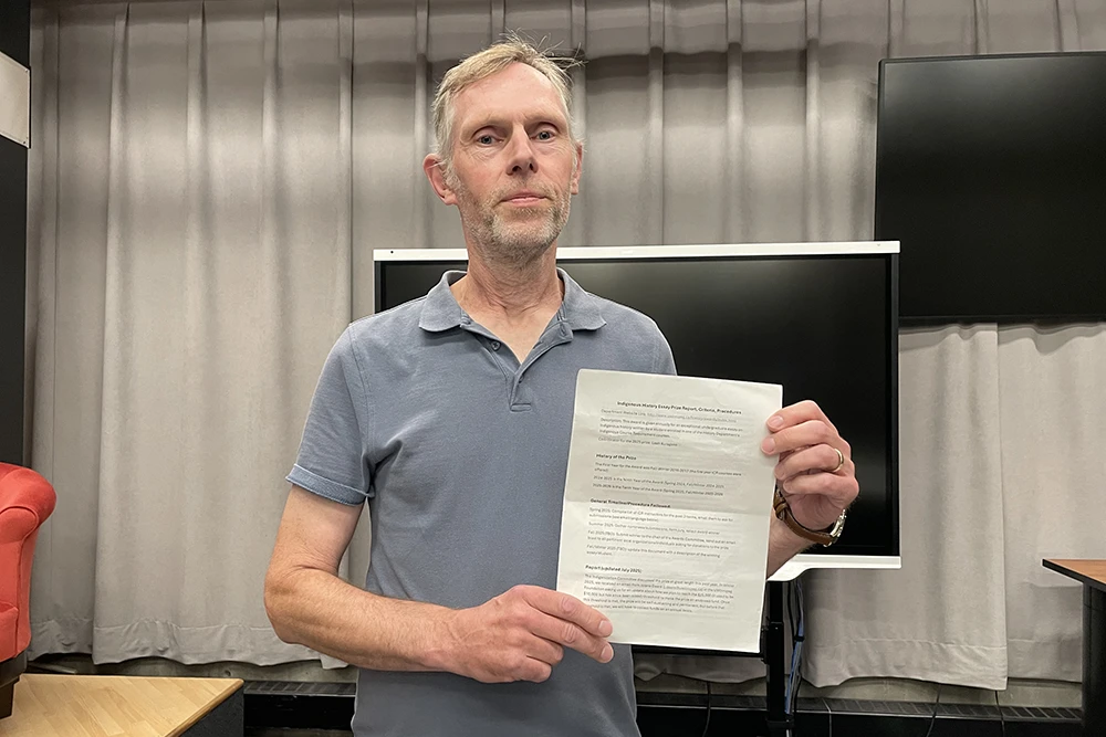 Mark Meuwese standing in front a screen holding a document