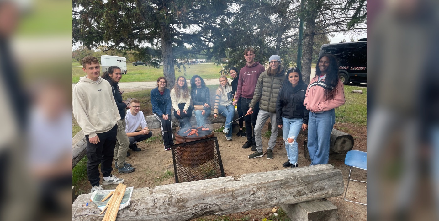 Several people stand around a campfire.