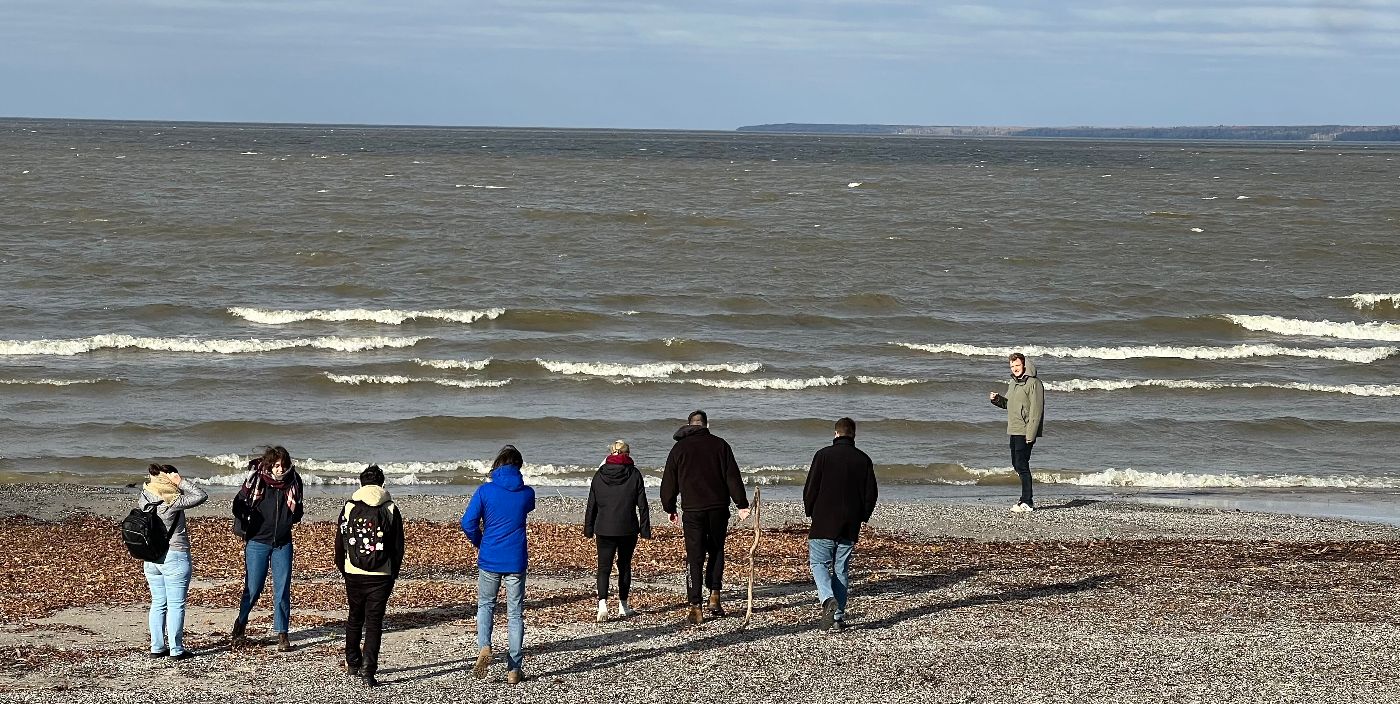 From a distance, several people are seen facing the water of Lake Winnipeg as waves roll in.